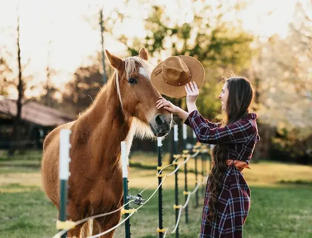 Disadvantages Of Horse Riding For Females. An image of a woman presenting her hat to a horse. 
